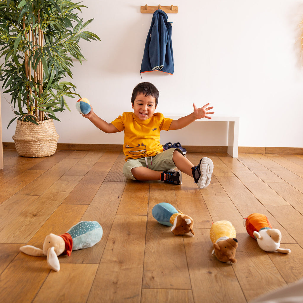 Uśmiechnięty chłopiec bawi się Zestawem miękkich Kręgli dla dzieci. Pluszowe kręgle-zwierzątka i piłeczka rozwijają motorykę i zmysły w formie radosnej gry.