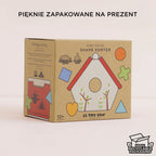 Eleganckie, ekologiczne opakowanie drewnianego sortera kształtów domek dla ptaków Le Toy Van, idealne na prezent. Brązowe kartonowe pudełko z barwną grafiką domku i informacjami o zrównoważonym drewnie, braku plastiku oraz 100% recyklingu. Wskazuje wiek 12+ miesięcy.