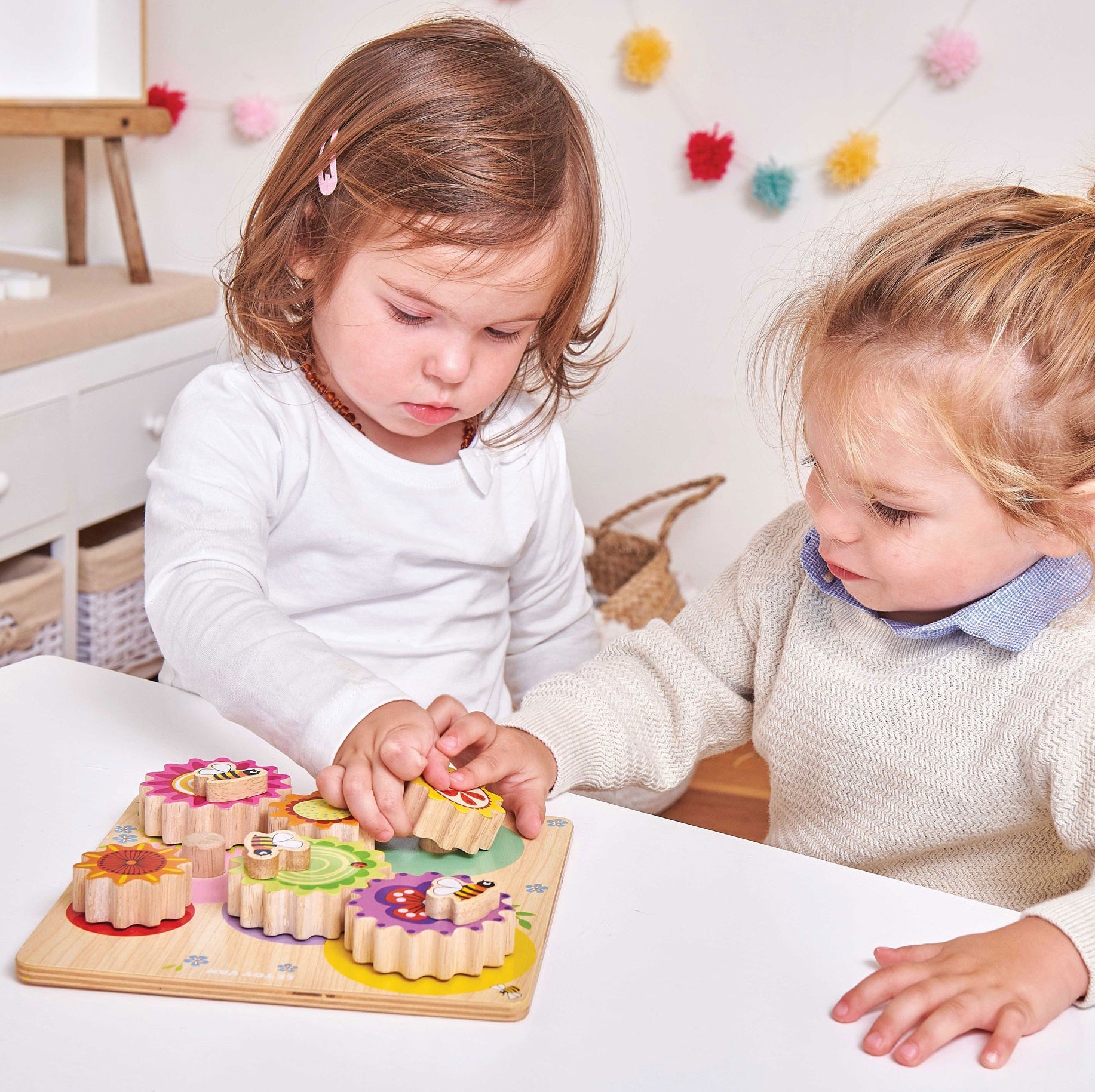 Dwoje dzieci z zaangażowaniem odkrywa drewniane kółka zębate – sensoryczną zabawkę edukacyjną z kolorowymi pszczołami, kwiatami i słońcem, wspierającą rozwój poznawczy i naukę mechanizmów.