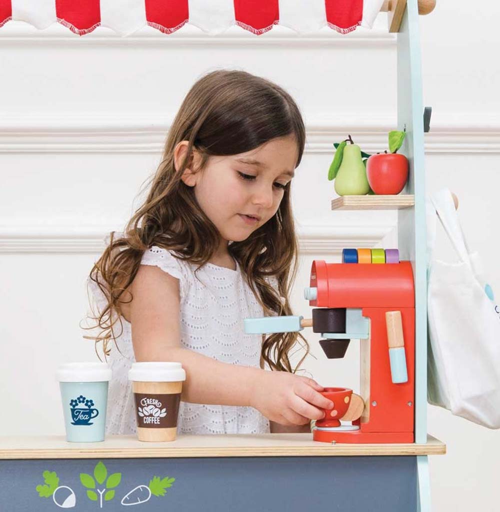 Dziewczynka bawi się realistycznym drewnianym ekspresem do kawy, nalewając kawę do filiżanki. Idealne akcesoria kuchenne dla małych baristów i kreatywnej zabawy w domową kawiarnię.