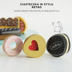 Trzy urocze, bogato zdobione drewniane ciasteczka zabawki: różowy pączek, żółte ciastko serce z czerwoną wstawką oraz ciemne ciastko typu sandwich z napisem 'Cookie'. Wykonane z bezpiecznego drewna i pastelowych, nietoksycznych farb.