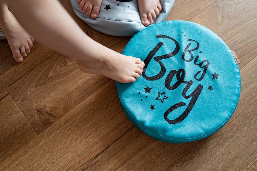 Okrągła poduszka ekoskóra BIG BOY turkusowa z nadrukiem, na której bawią się dziecięce stopy, idealna do pokoju malucha.