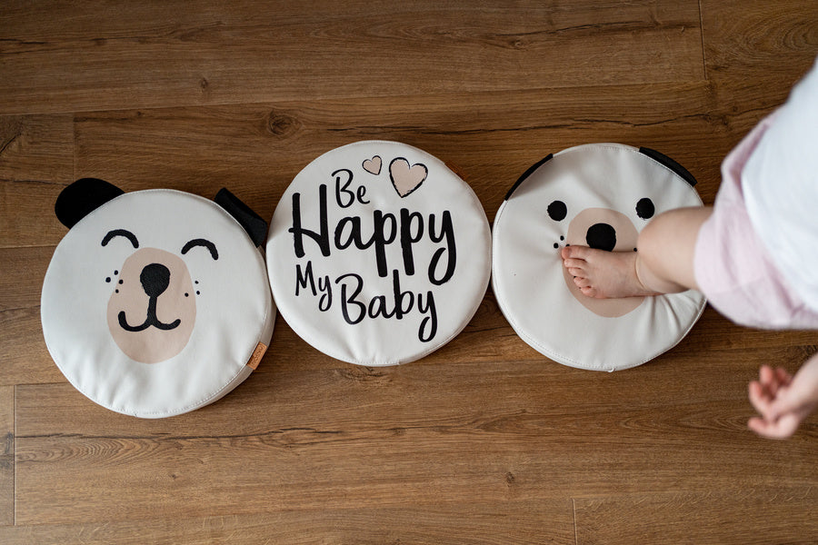 Białe poduszki z ekoskóry MIŚ z uszkami i napisem 'Be Happy My Baby'. Dziecięca stópka na podłodze, idealne do pokoju dziecka.
