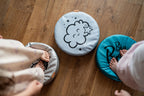 Zestaw 3 okrągłych poduszek z ekoskóry LITTLE PRINCESS o grubości 6 cm, z motywami chmurki i gwiazdki, na których dzieci bawią się na drewnianej podłodze. Idealne do pokoju dziewczynki.