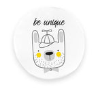 Okrągła poduszka z ekoskóry dla dzieci, biała, z motywem uroczego misia w czapce i inspirującym napisem „be unique”. Ożywia pokój dziecięcy.