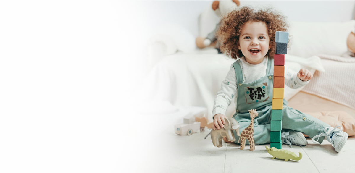 Szczęśliwe dziecko bawi się kolorowymi drewnianymi klockami i figurkami zwierząt. Odkryj ekologiczne zabawki edukacyjne Montessori dla kreatywnego rozwoju malucha.